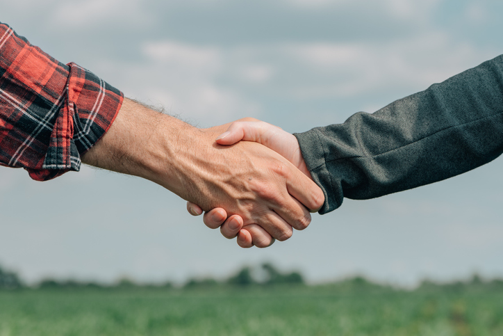 Mortgage loan officer and farmer shaking hands upon reaching an agreement for financial allowance application, banker and farm worker in corn maize crop field.